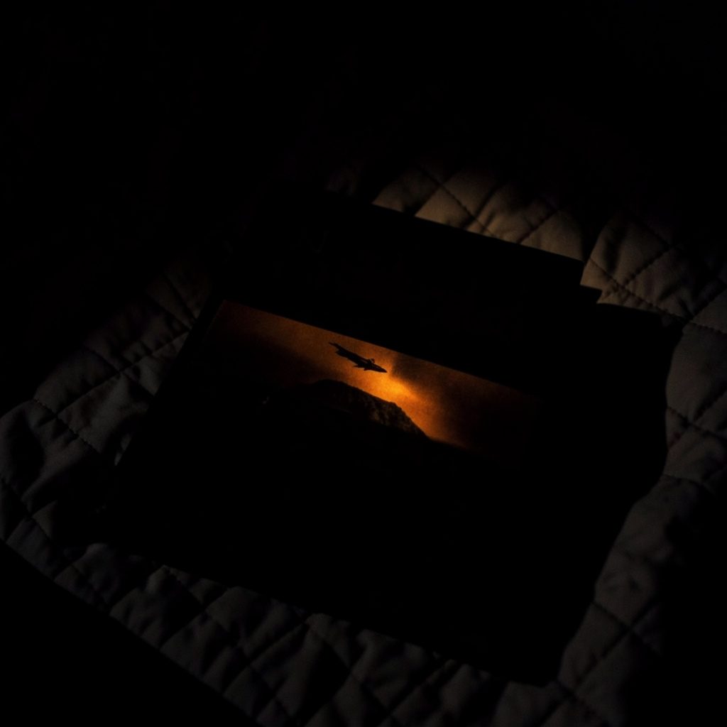 A dark, low-key photograph of a historical fiction novel resting on a quilt, deep shadow enveloping the scene with a narrow band of warm light across the cover.